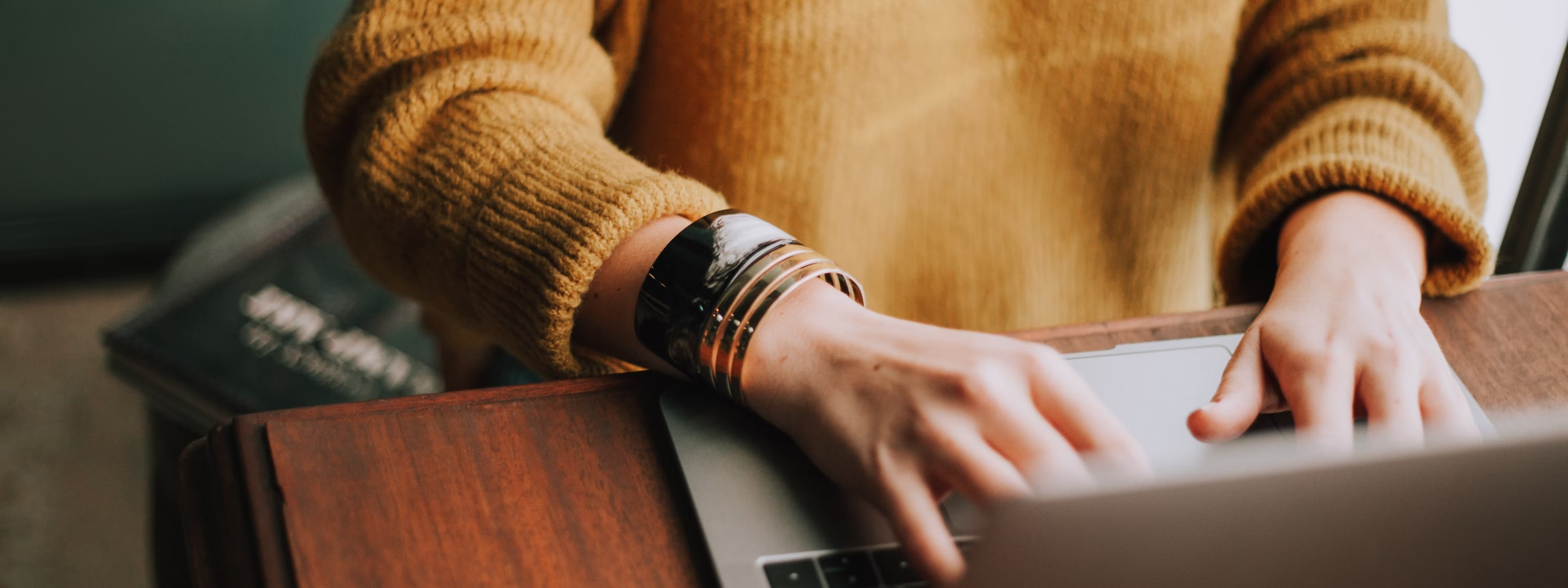 Person in yellow sweater typing on laptop with smartwatch