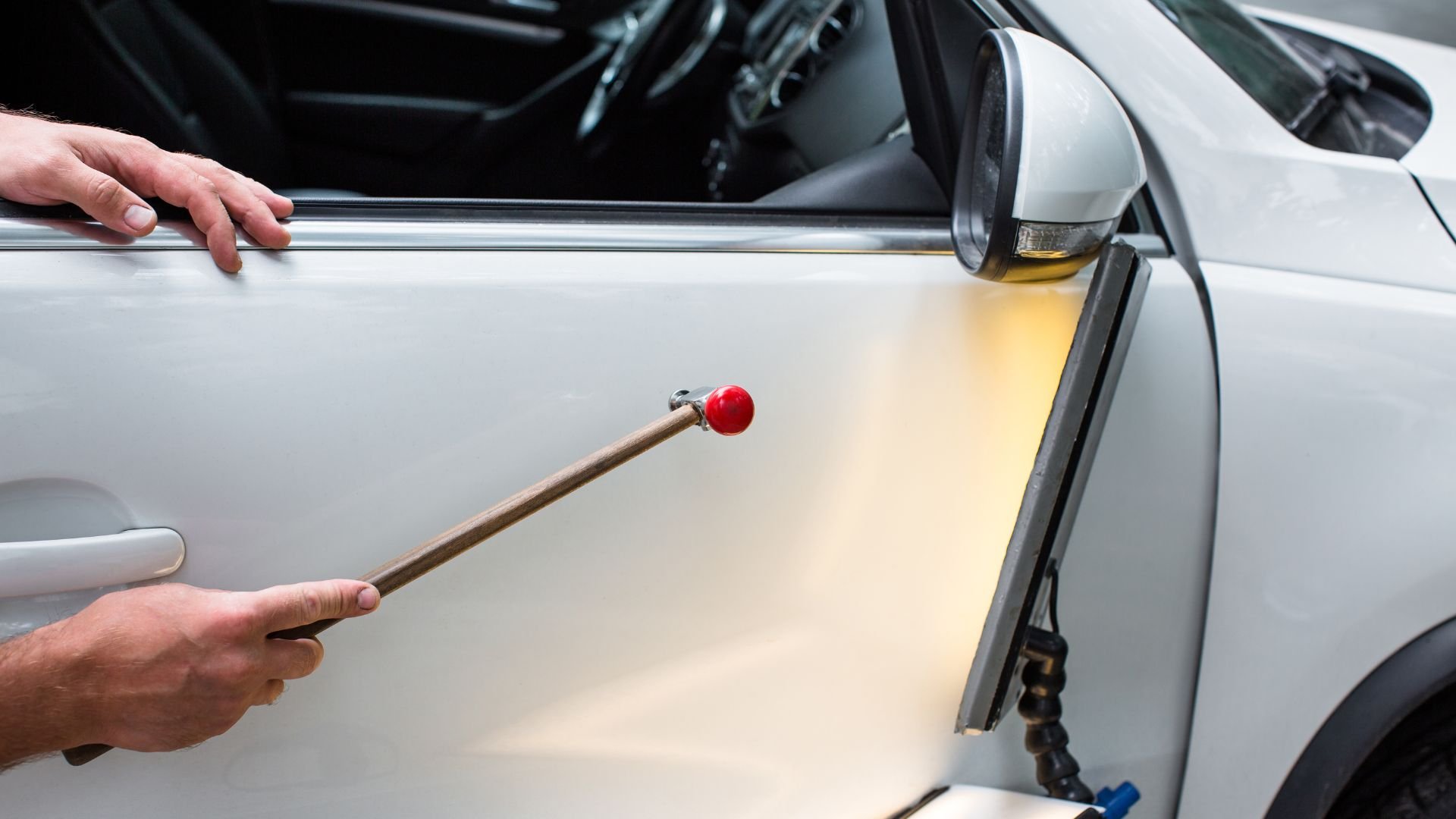 Person using long rod with red ball to tap white car door
