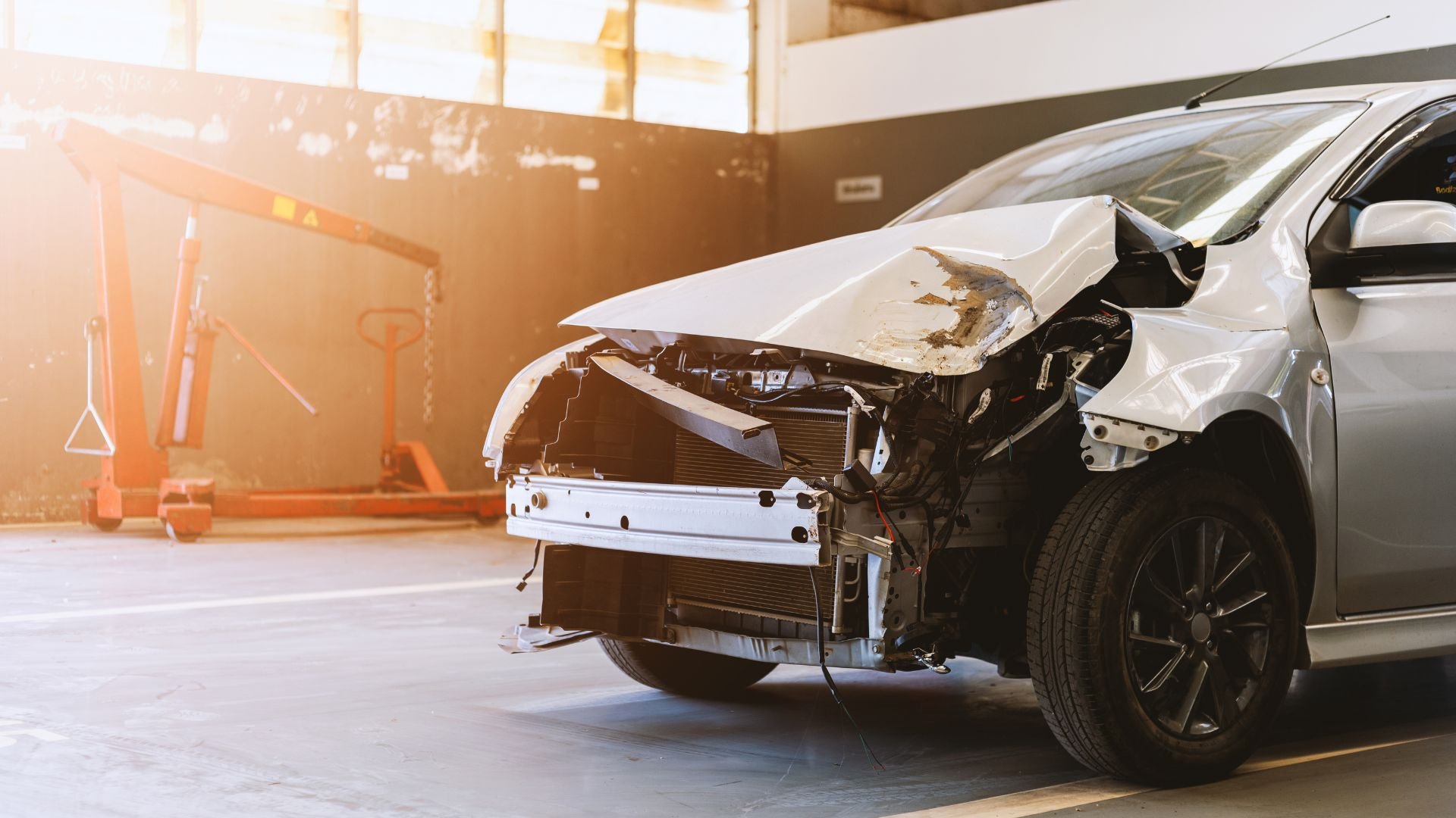 Severely damaged white car with front end crushed in auto repair shop