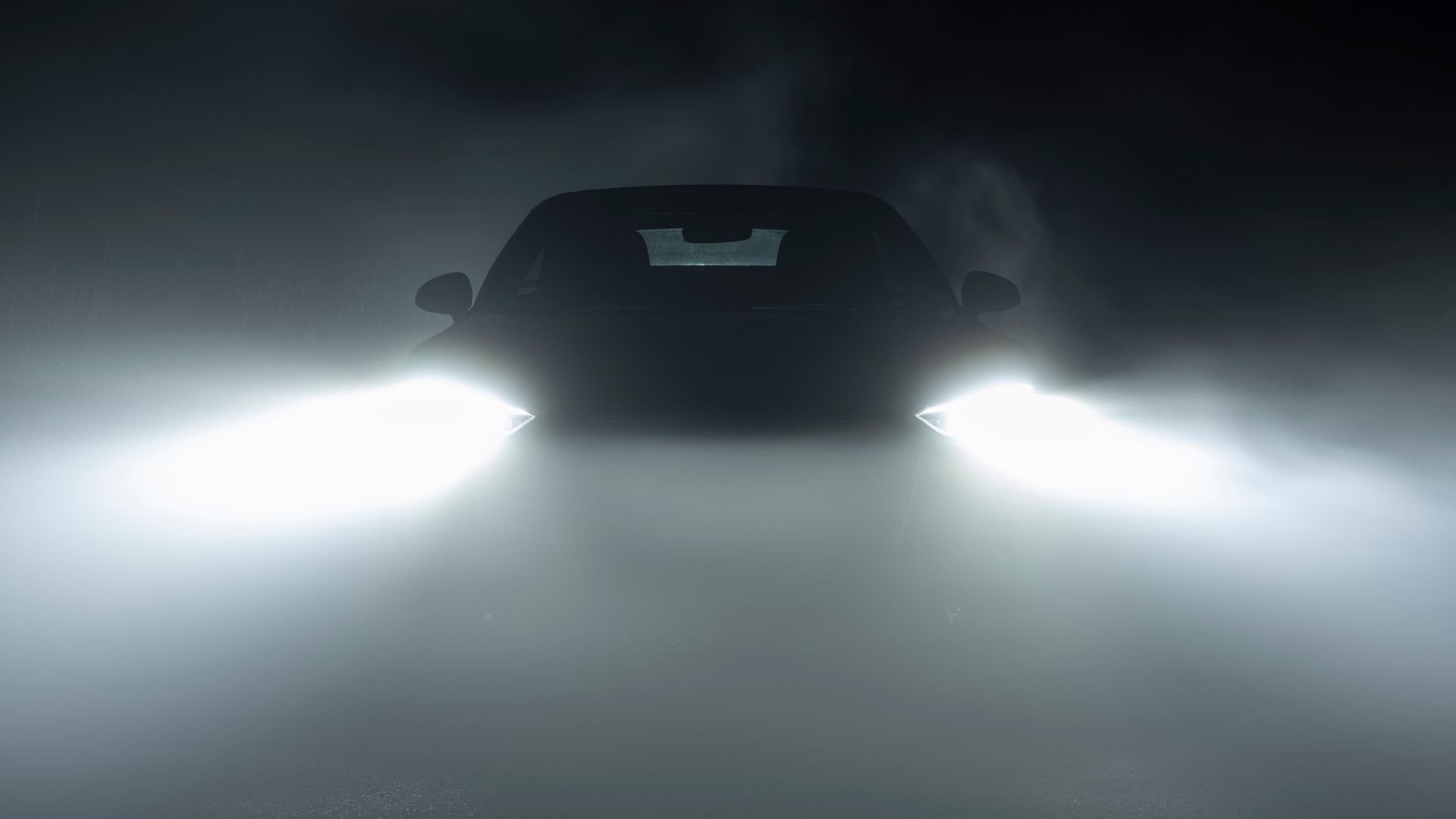 Car silhouette with bright headlights shining through misty atmosphere
