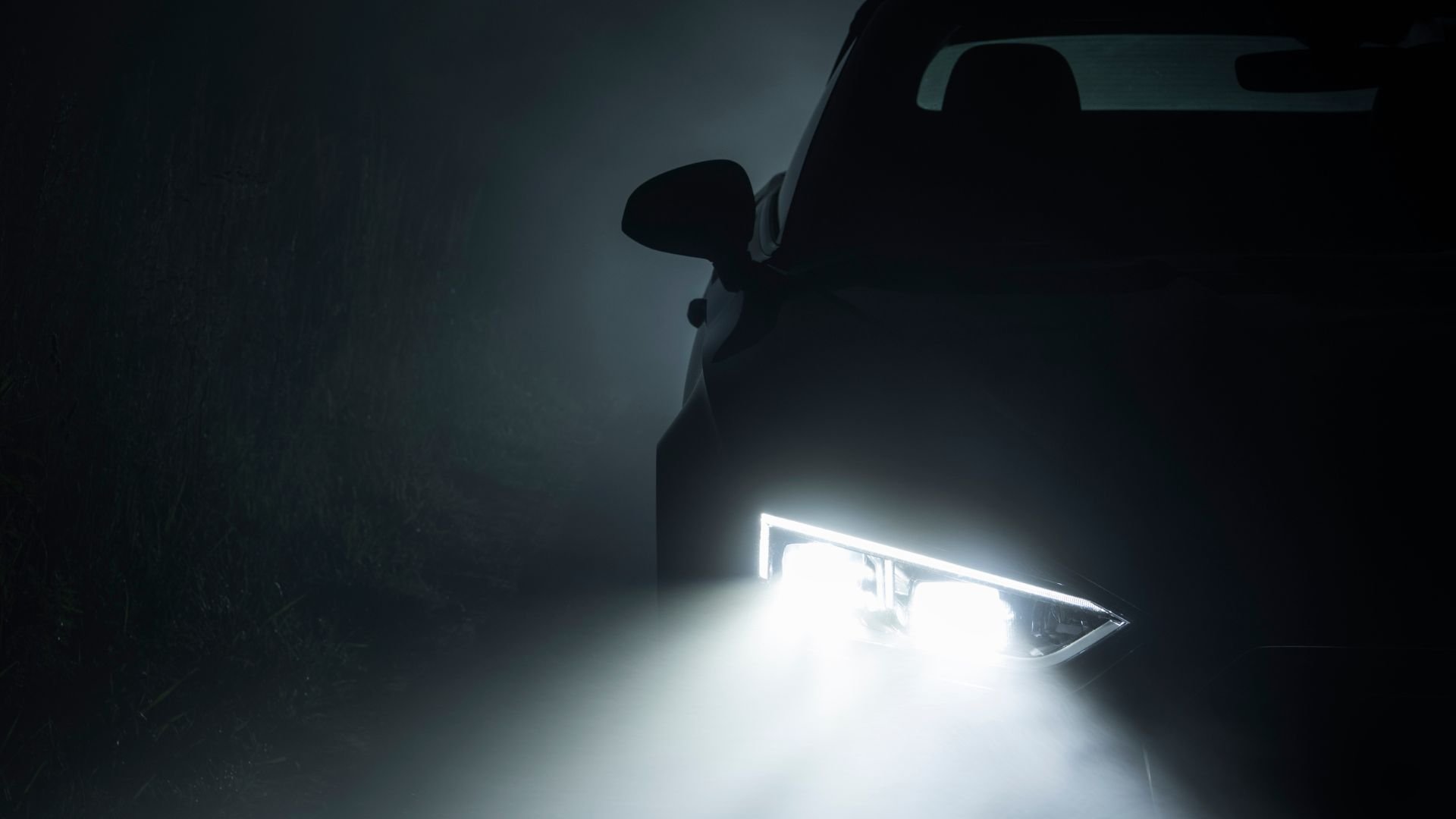 Bright headlight illuminating dark silhouette of car at night