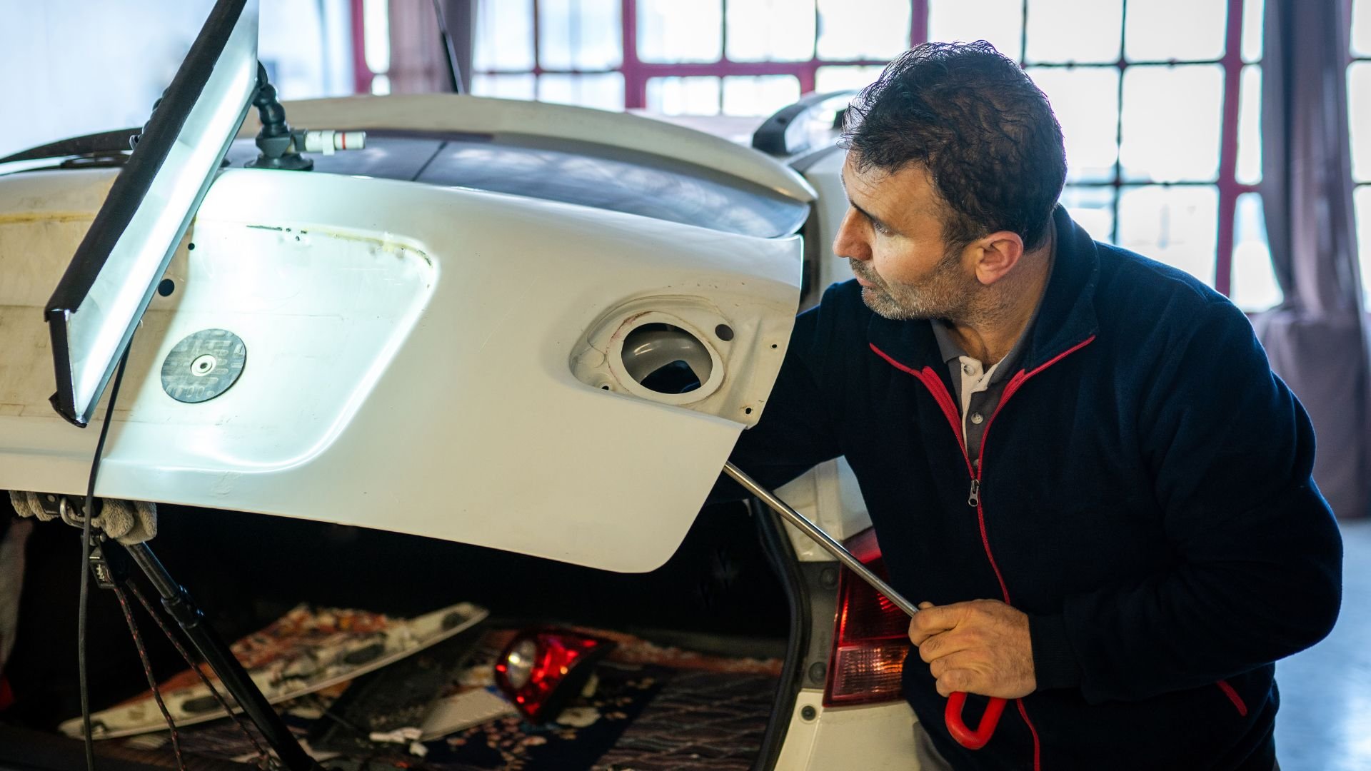 Mechanic examining open car hood in workshop with focused expression