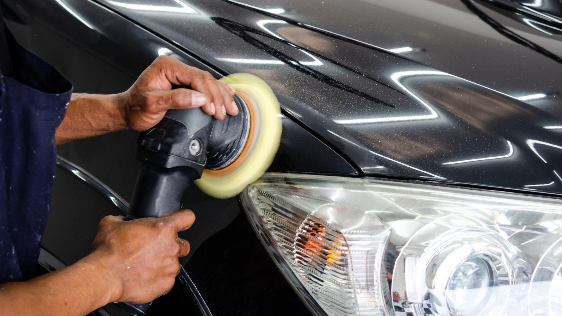 Polishing black car with orbital buffer near headlight