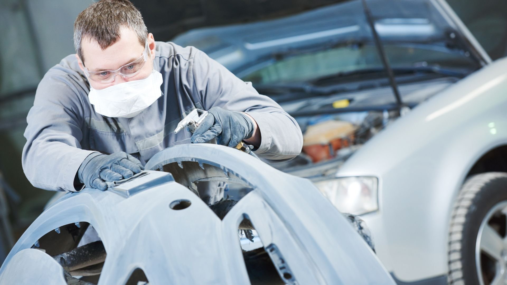 Auto body worker sanding car part with protective mask and goggles