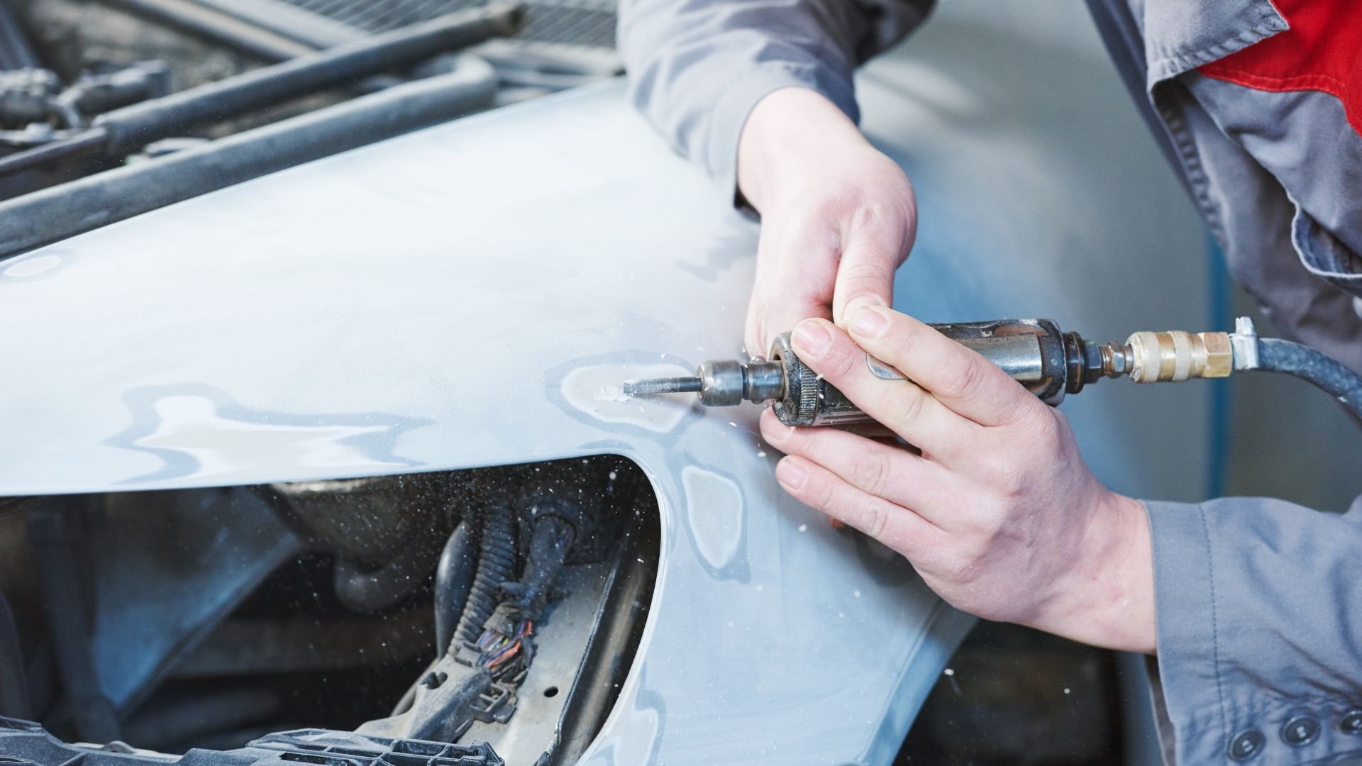 Auto repair technician using pneumatic drill on vehicle body panel
