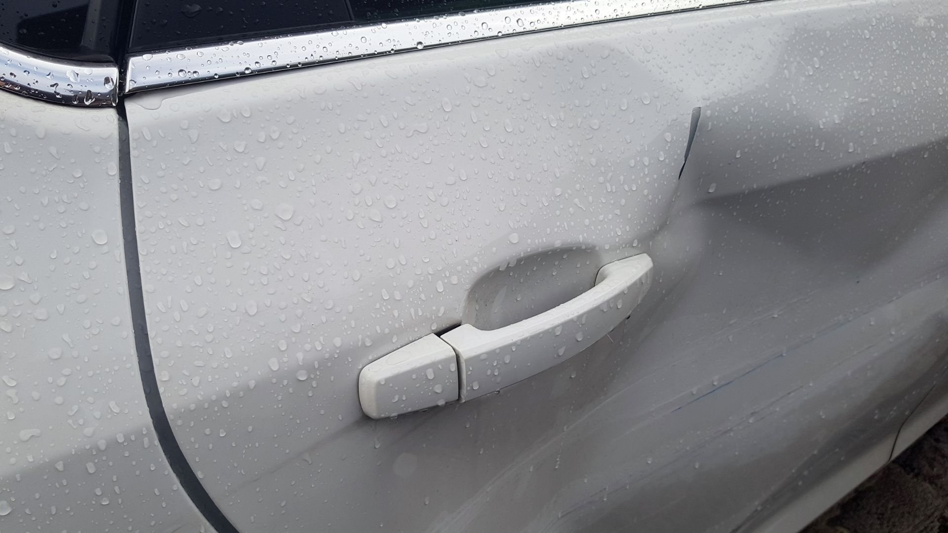 White car door handle with water droplets on rainy day