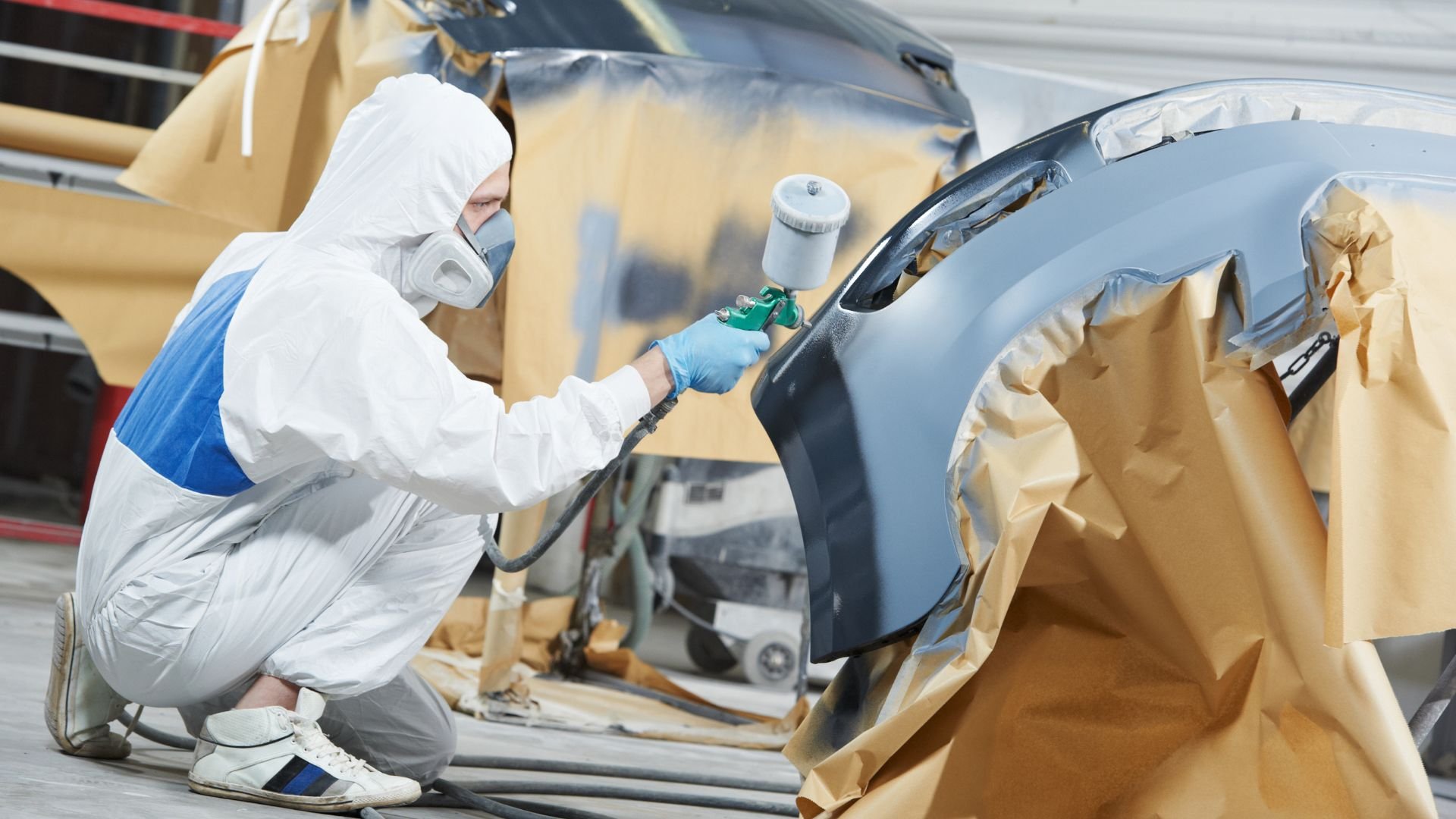 Auto body worker in protective suit spray painting a car panel